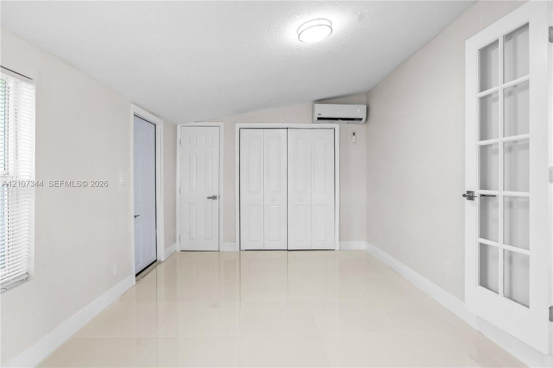 Neutral-toned interior featuring large-format tile flooring, double-door closet cabinetry, wall-mounted ductless climate control unit, and a French-style door with glass paneling