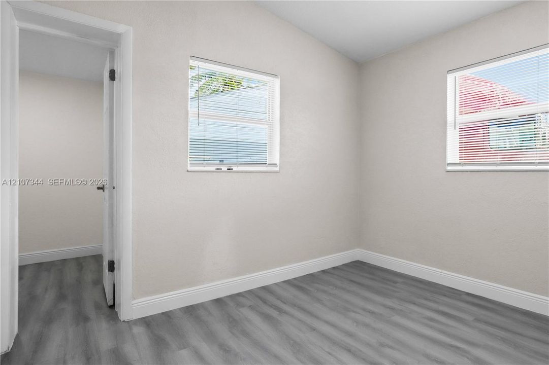 Interior room featuring neutral-toned walls, wood-finish flooring, and two windows with horizontal blinds