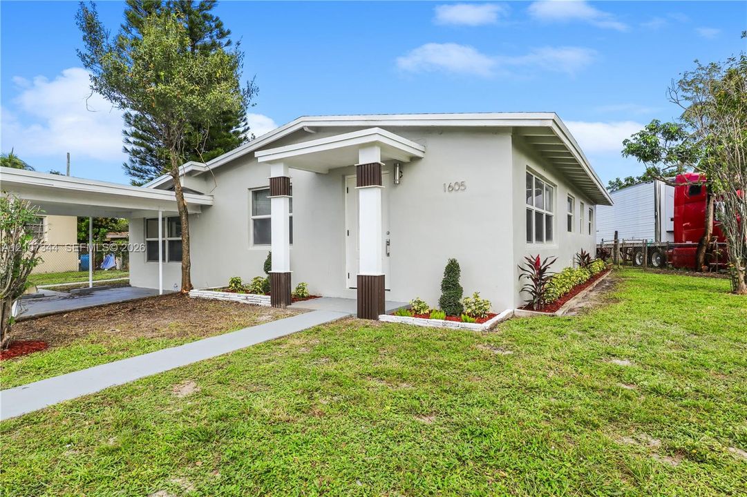 Single-story exterior featuring a covered entryway with decorative columns, a concrete walkway, a carport, and low-profile landscaping