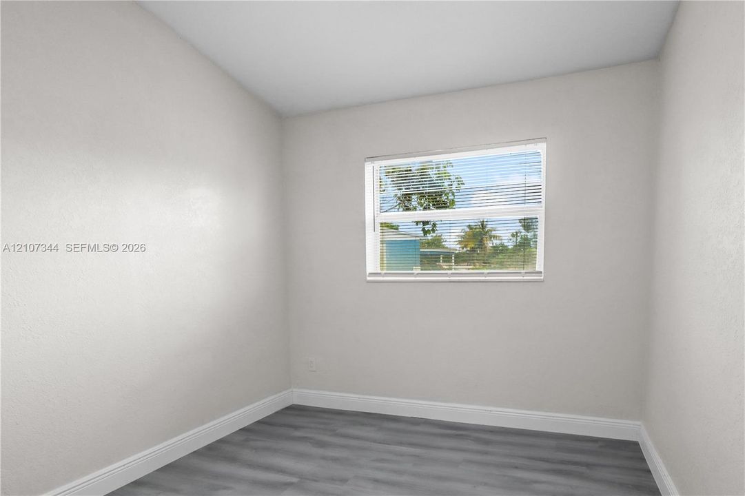 Interior room featuring neutral wall paint, wood-finish flooring, and a single-hung window with integrated horizontal blinds
