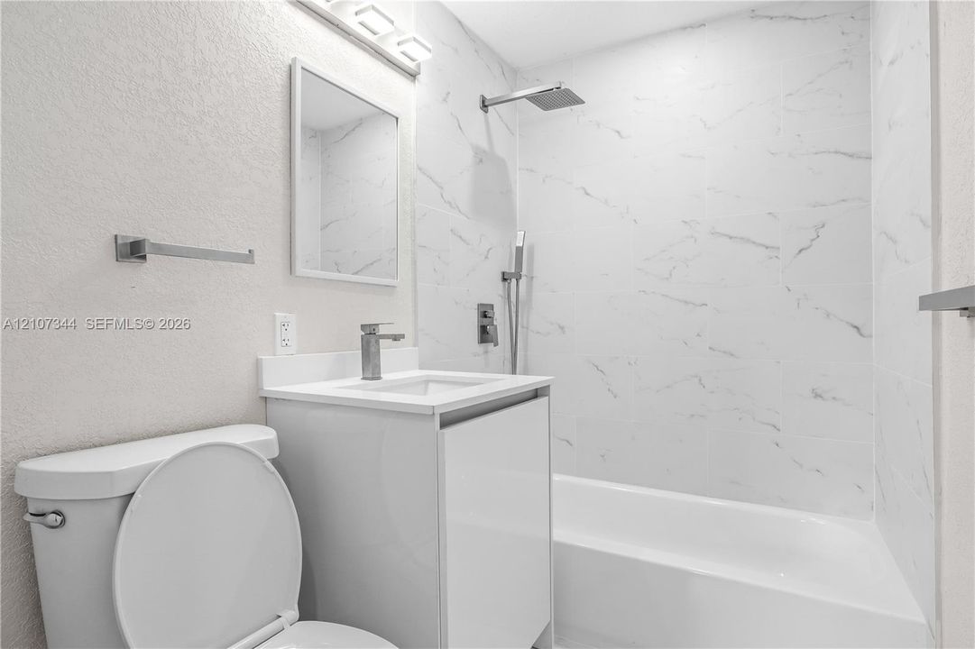 Bathroom featuring a vanity with a rectangular sink, stone-finish wall tiling in the shower area, a rain-style shower head with a handheld attachment, and a framed mirror