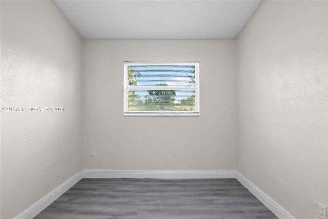 Interior space featuring neutral-toned walls, wood-finish flooring, and a central window with horizontal blinds