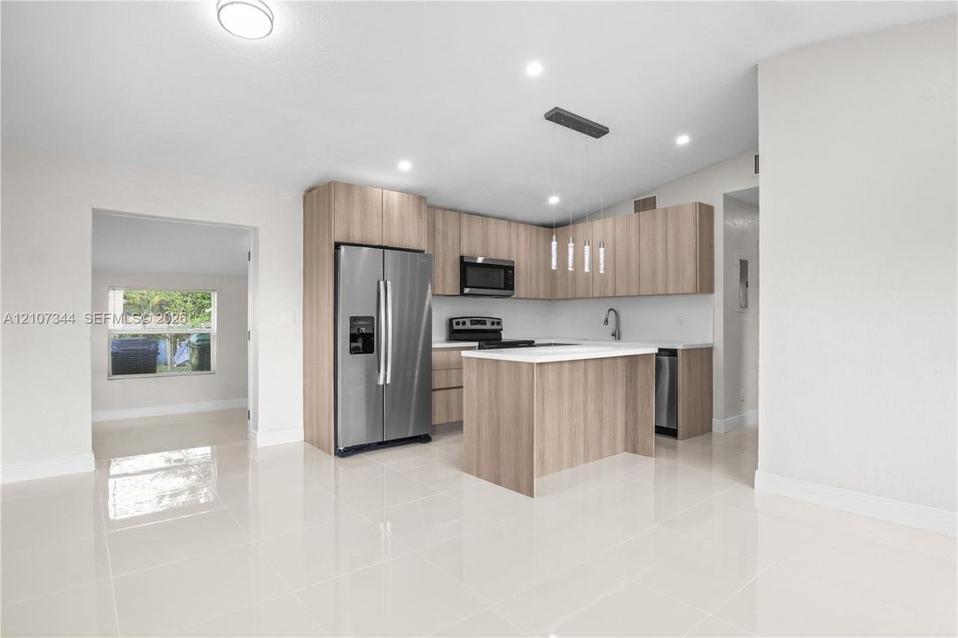 Kitchen featuring light-finish cabinetry, white countertops, central island, stainless steel appliances, and tile flooring