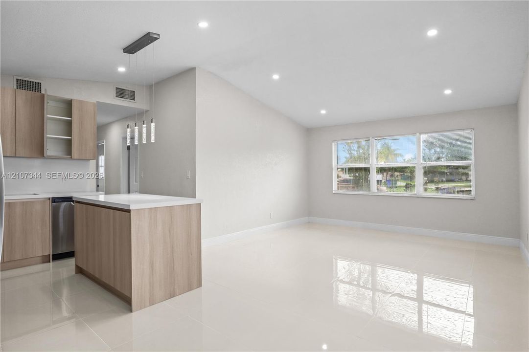Kitchen featuring light wood-finish cabinetry, a central island with a white countertop, polished tile flooring, recessed ceiling lighting, and large windows
