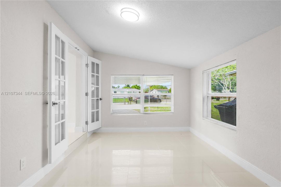 Bright sunroom featuring light-toned tile flooring, white-painted walls, dual French doors with glass panes, and large picture windows