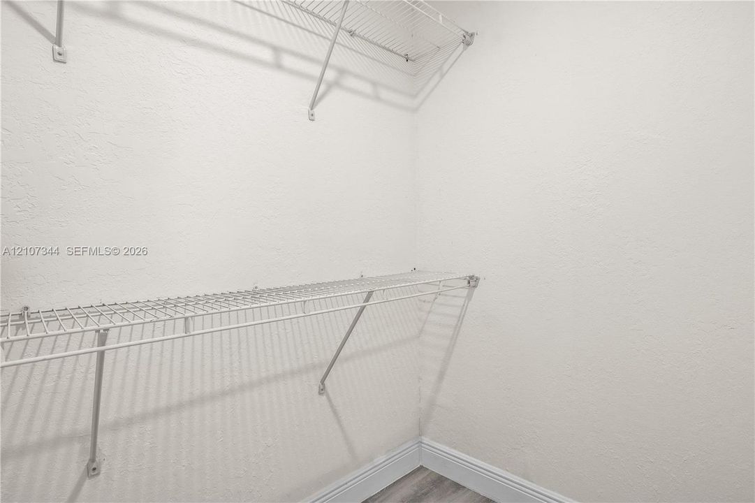 Storage area featuring white textured walls and dual-tier white wire shelving systems