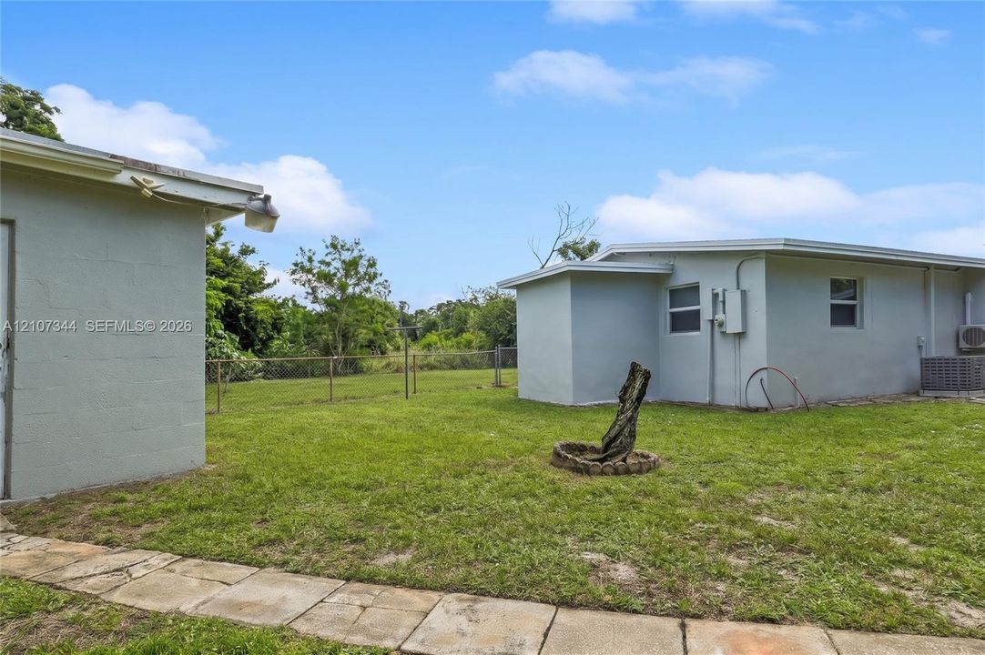 Backyard featuring concrete block structures, a grass lawn, a stone walkway, and chain-link fencing