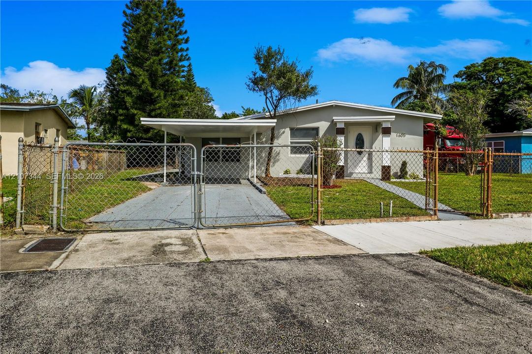 Exterior featuring a covered carport, chain-link perimeter fencing, gated driveway access, and a concrete walkway