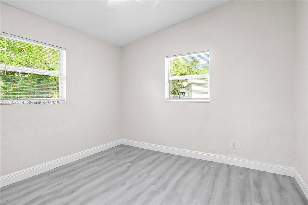 Neutral-toned interior space featuring vaulted ceilings, wood-finish flooring, and two windows with horizontal blinds