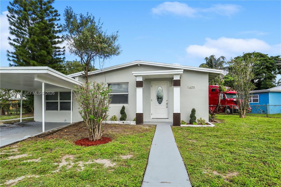 Single-story exterior featuring a concrete walkway, attached carport, covered entryway with decorative columns, and an inset glass-panel front door