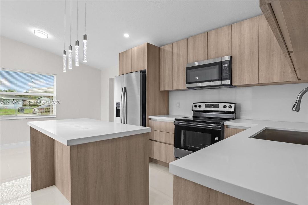 Kitchen featuring light wood-finish cabinetry, white countertops, stainless steel appliances, and a central island with pendant lighting
