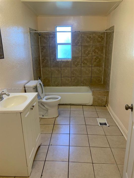Bathroom featuring a white vanity cabinet with an integrated sink, floor-to-ceiling tile surrounding the tub, a built-in tile tub bench, and neutral floor tiling