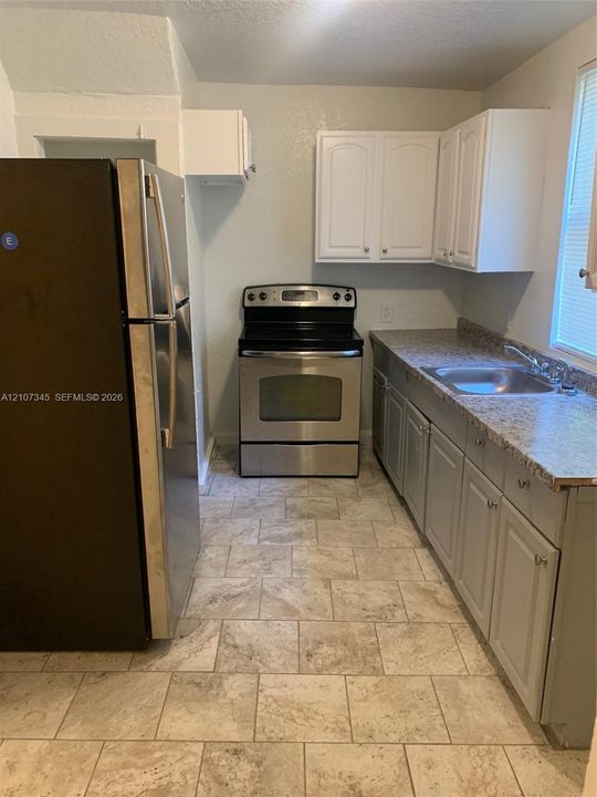 Kitchen featuring stainless steel appliances, speckled stone-finish countertops, tiled flooring, and dual-tone cabinetry