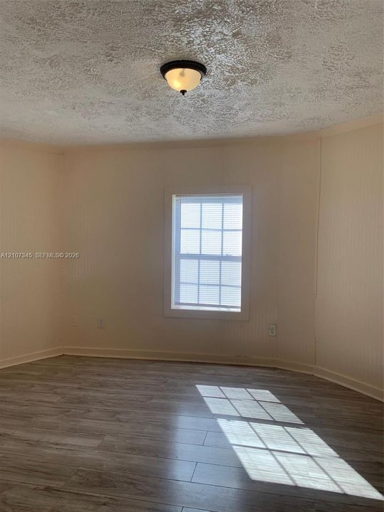 Room featuring wood-finish flooring, textured ceiling, single window with grid detailing, and flush-mount light fixture