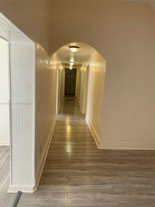 Hallway featuring an arched entryway, wood-finish flooring, and flush-mount ceiling lighting