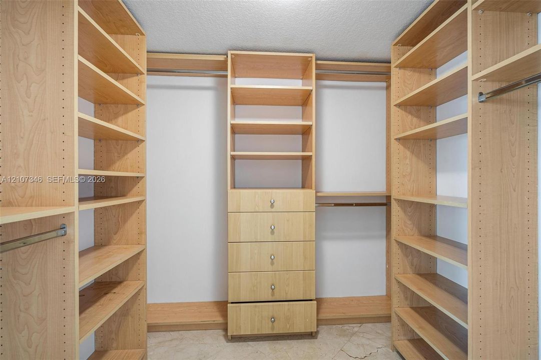 Custom-built closet featuring adjustable wood-finish shelving, integrated clothing rods, five-drawer cabinetry with metal pulls, and tile flooring