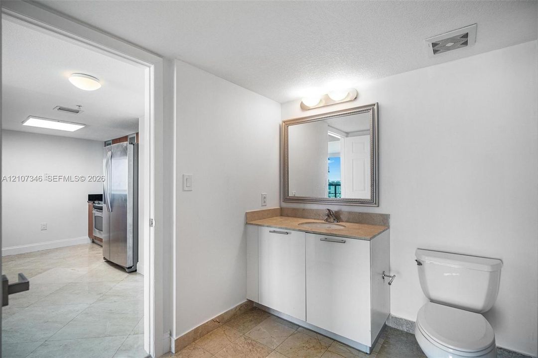 Bathroom featuring a white vanity cabinet, neutral solid-surface countertop, rectangular mirror, and porcelain tile flooring
