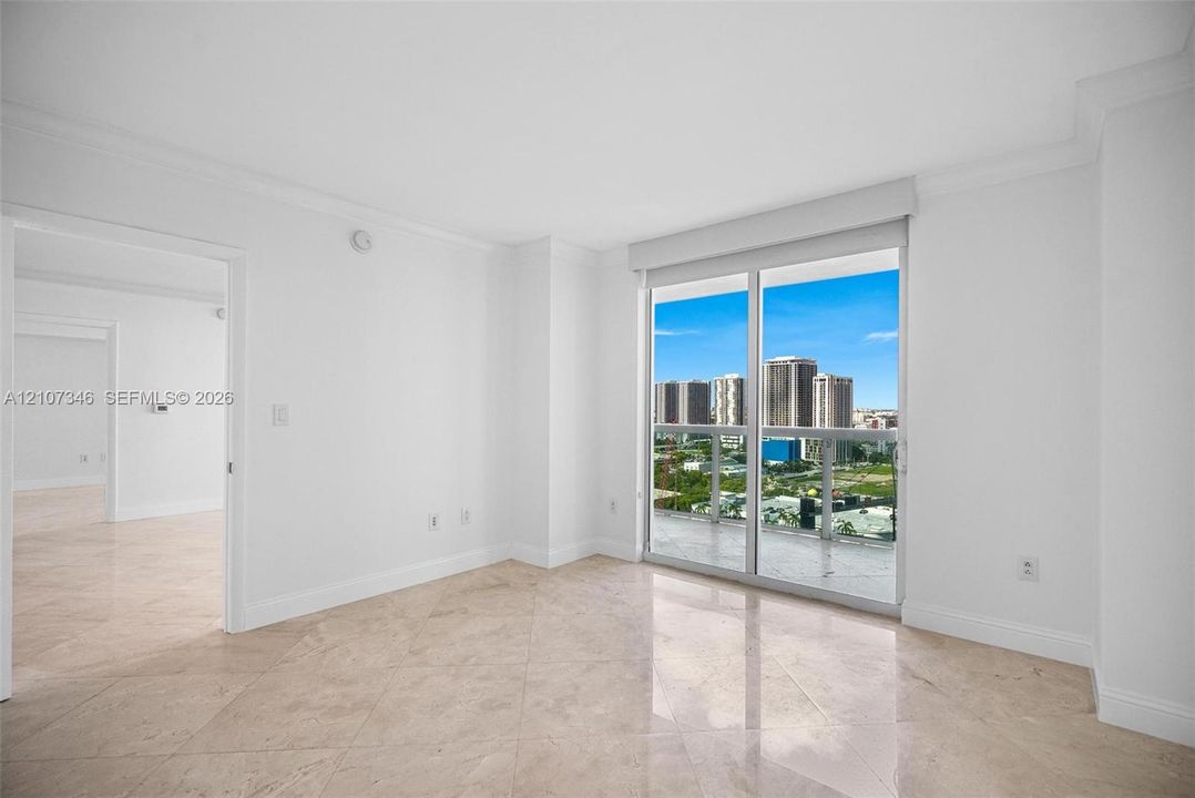 Neutral-toned stone flooring, sliding glass door, glass-paneled balcony railing, and high-rise exterior backdrop