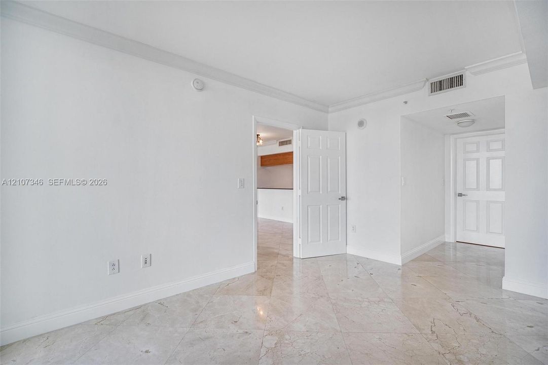 Interior space featuring polished stone tile flooring, six-panel interior doors, and crown molding