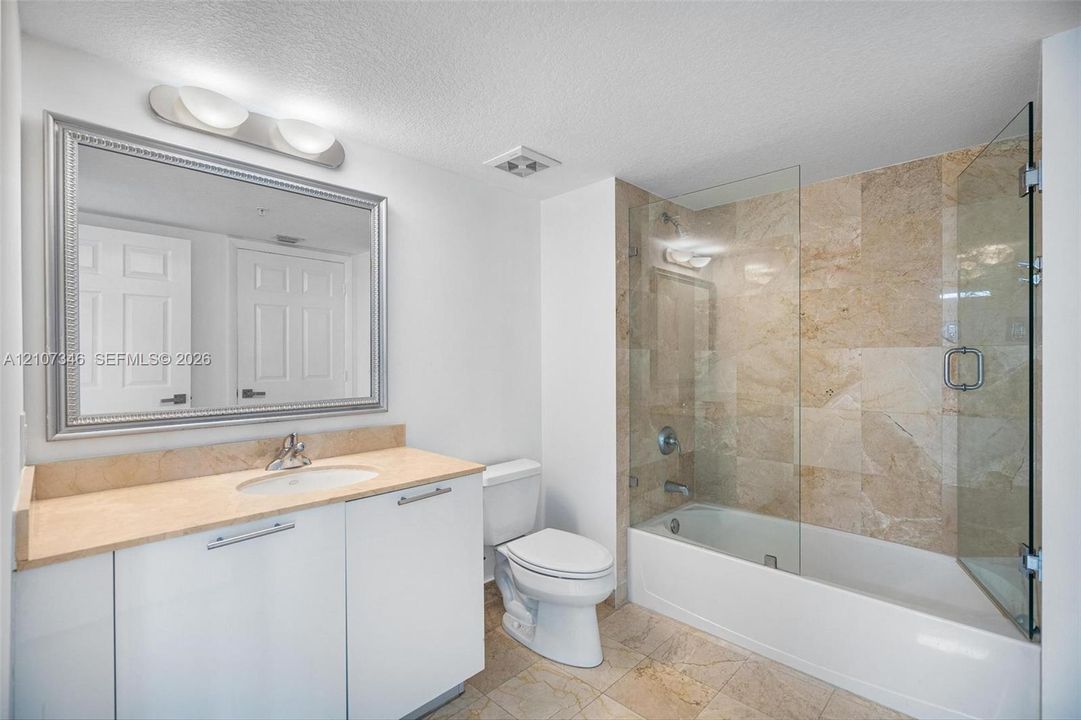 Bathroom featuring a stone-topped vanity with an integrated sink, a framed wall mirror, and a tiled shower-tub combination enclosed by a glass panel