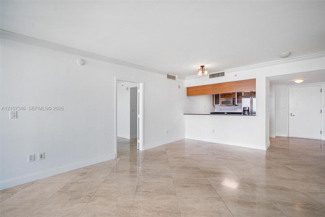 Open-concept interior featuring large-format tile flooring, a kitchen pass-through counter, wooden upper cabinetry, and crown molding