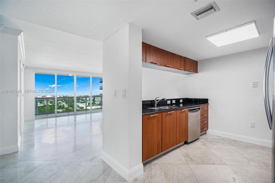 Kitchen featuring natural wood-finish cabinetry, dark stone countertops, stainless steel appliances, and large-format tile flooring, complete with floor-to-ceiling windows