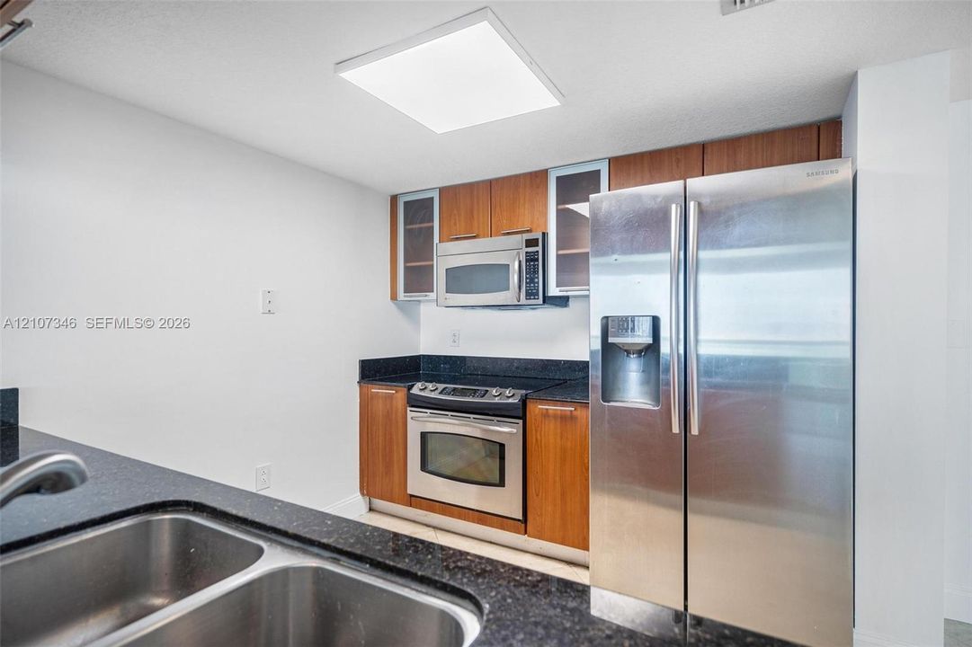 Kitchen featuring wood cabinetry with glass-panel accents, dark stone-style countertops, stainless steel appliances, and a dual-basin undermount sink