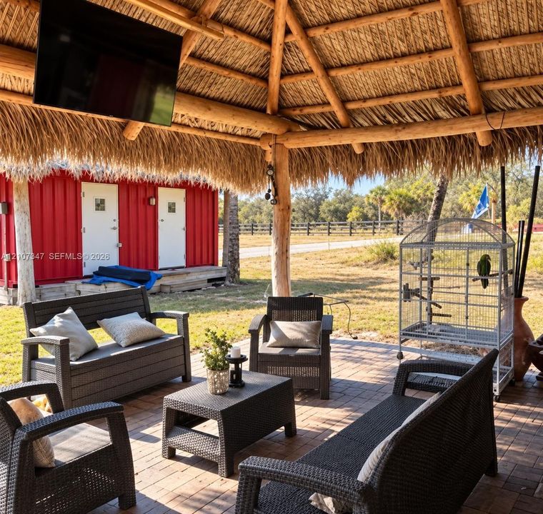 Open-air palapa structure featuring a thatched roof, exposed timber post-and-beam construction, and integrated flat-screen television mount, set atop a paved brick patio