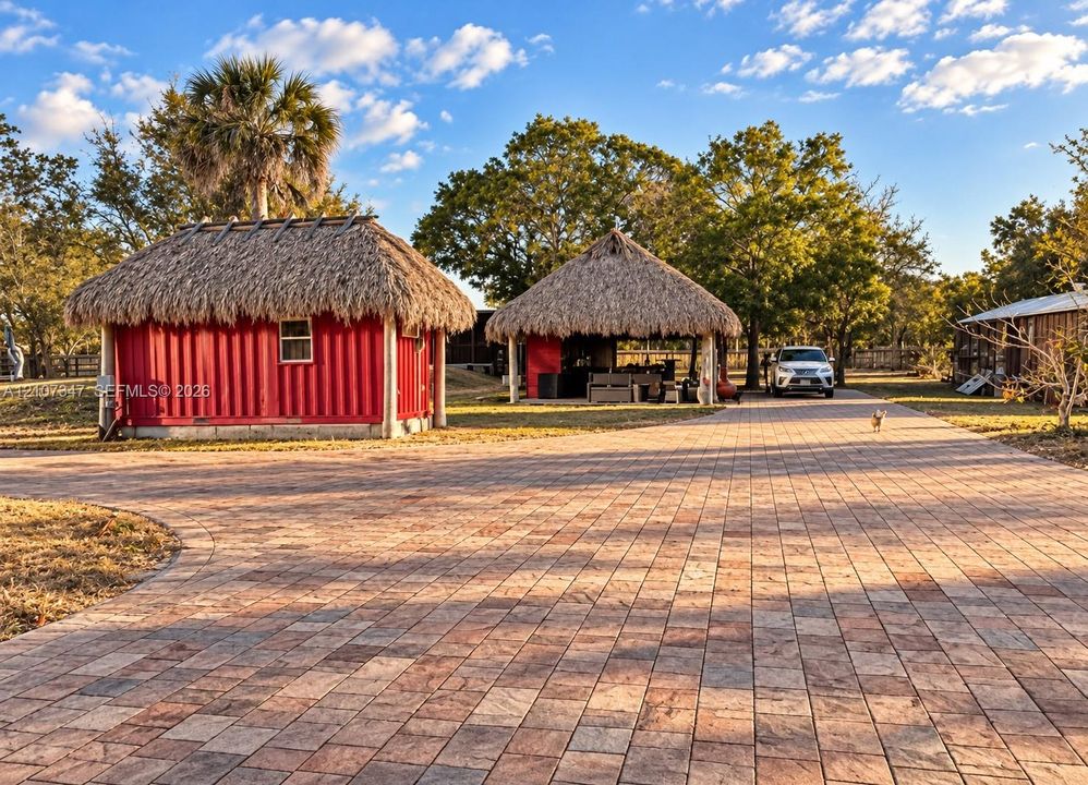 Extensive stone paver driveway leading to two structures featuring thatched roof designs