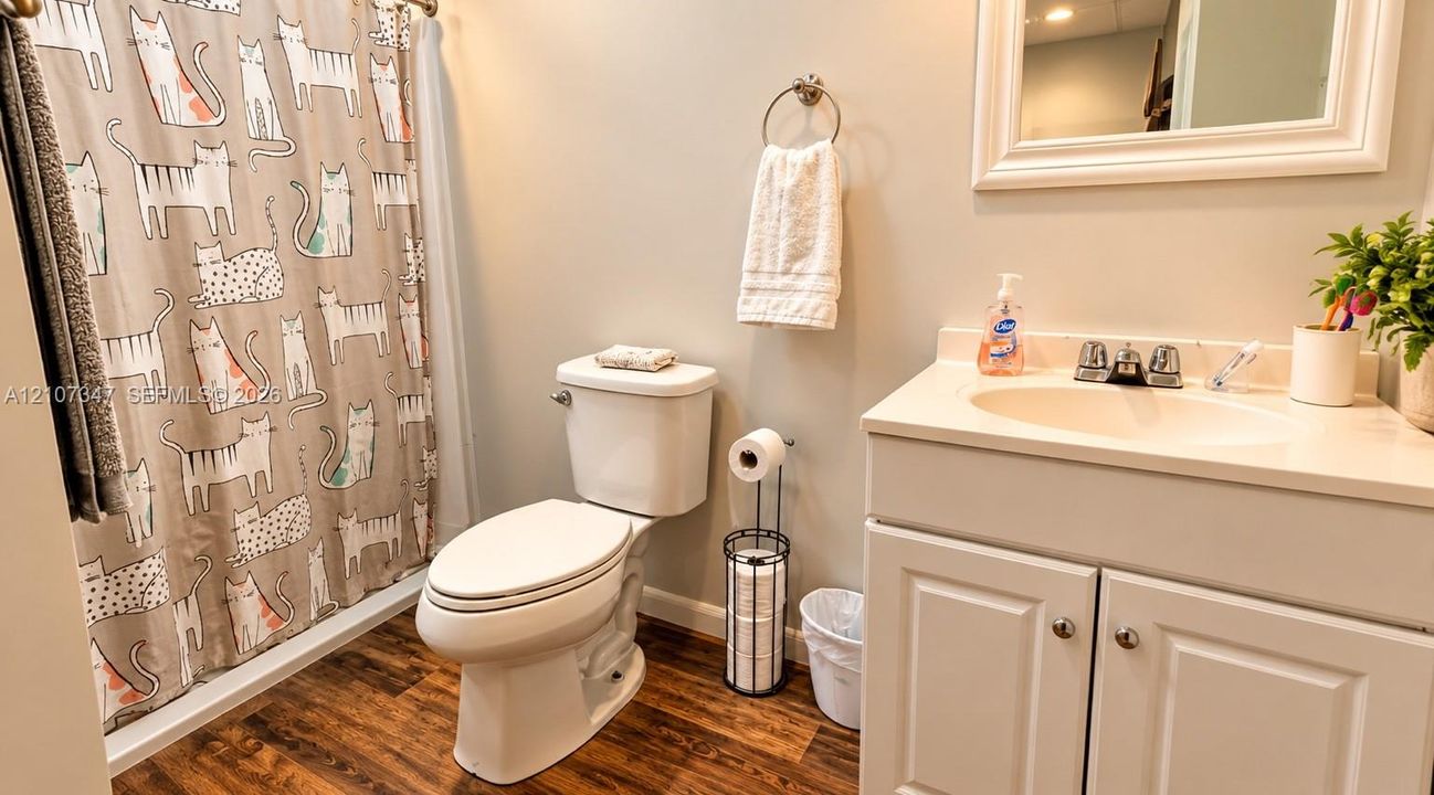 Bathroom featuring a white vanity cabinet with an integrated sink, a two-handle chrome faucet, a framed wall mirror, and wood-finish flooring