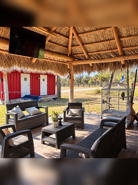 Covered patio with a natural thatched roof, exposed timber support beams, and paver flooring