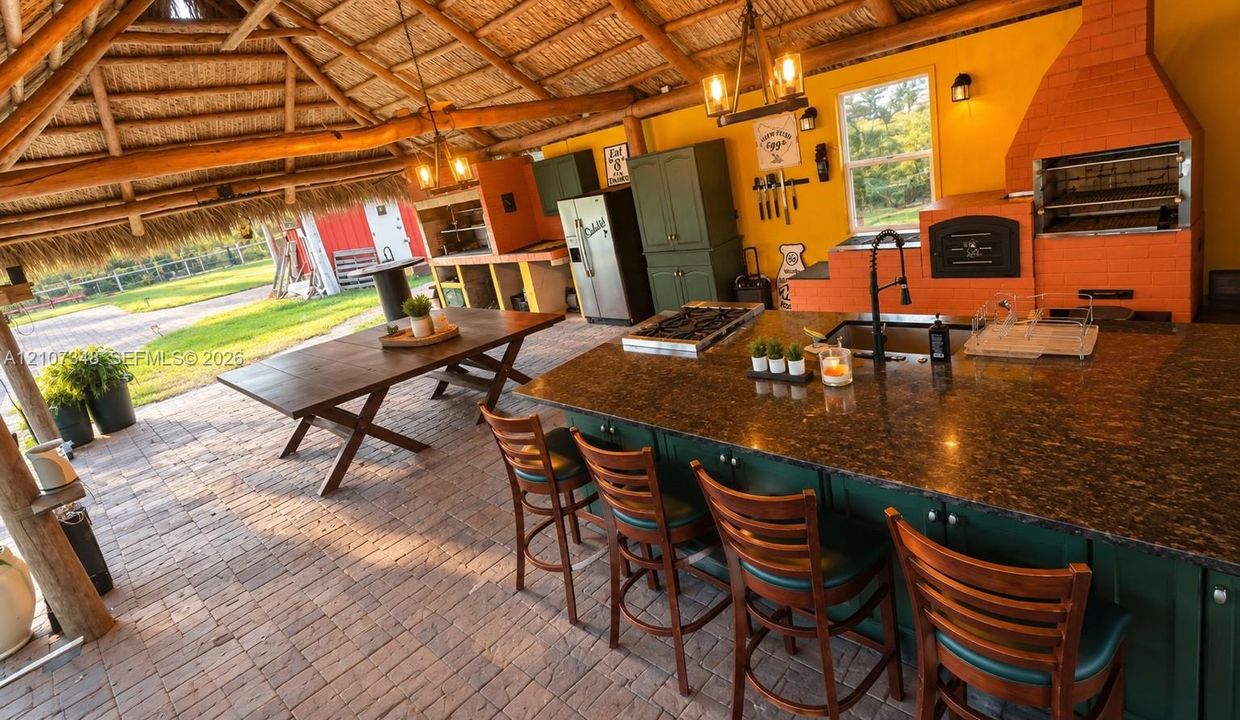 Outdoor kitchen featuring a thatched roof, brick paver flooring, built-in masonry grill, center island with stone countertop, and wood-finish cabinetry