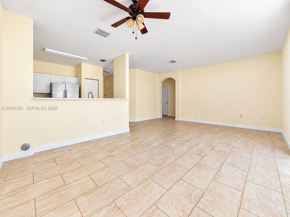 Open interior featuring ceramic tile flooring, a multi-blade ceiling fan with integrated lighting, and a breakfast bar overlooking white cabinetry