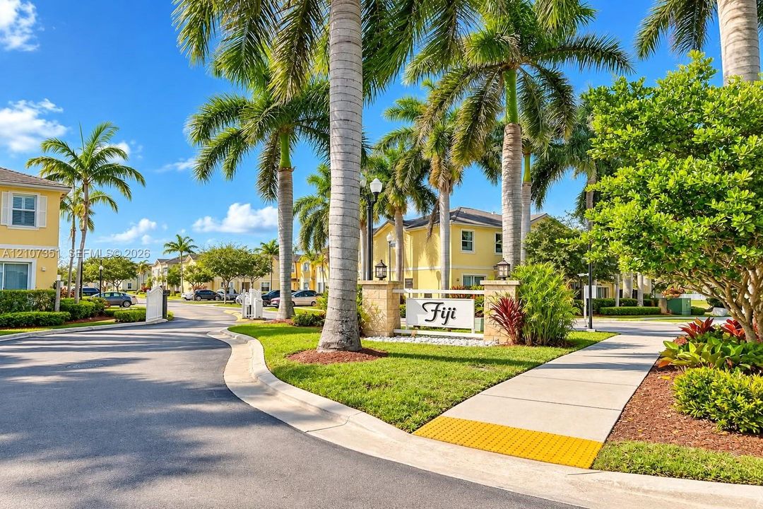 Community entrance featuring stone pillars, mature palm trees, paved thoroughfare, and landscaped grounds