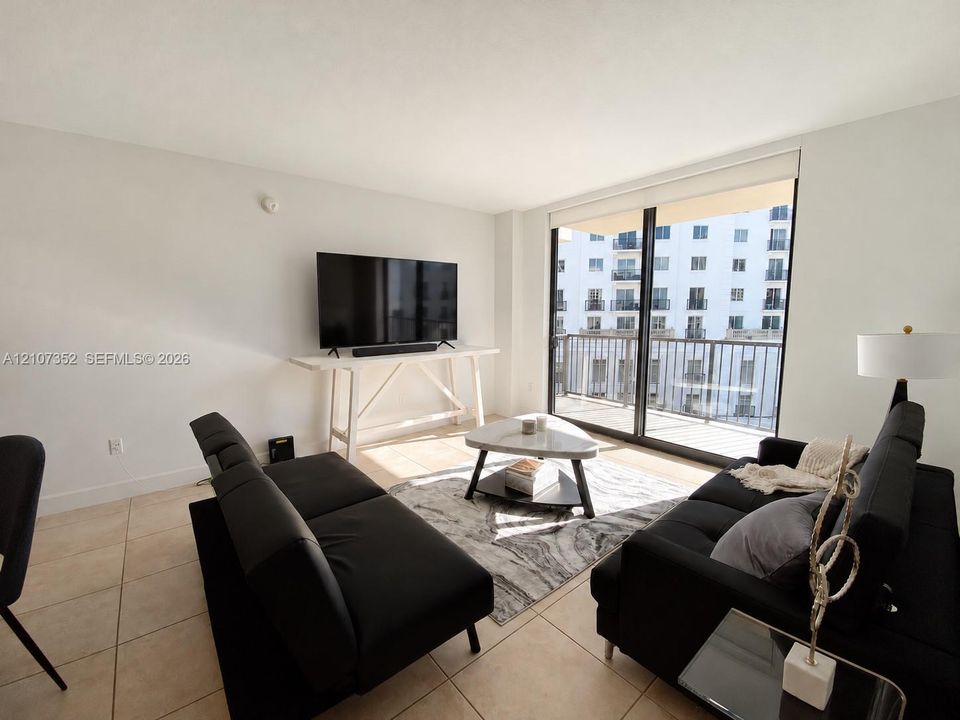 Living area featuring large-format tile flooring, floor-to-ceiling glass sliding doors, and a private balcony with metal railing