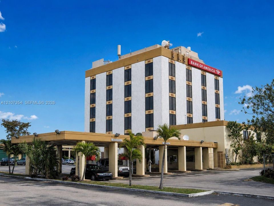 Five-story commercial office structure featuring a reinforced concrete facade, vertical glass paneling, and a covered drive-through arrival area with structural pillars