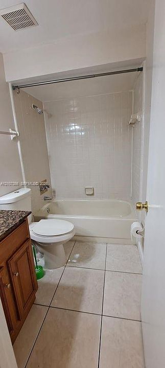 Hallway Bathroom featuring large-format floor tile, a wood-finish vanity with a stone-top surface, a combination tub and shower with tile surround, and a chrome shower fixture