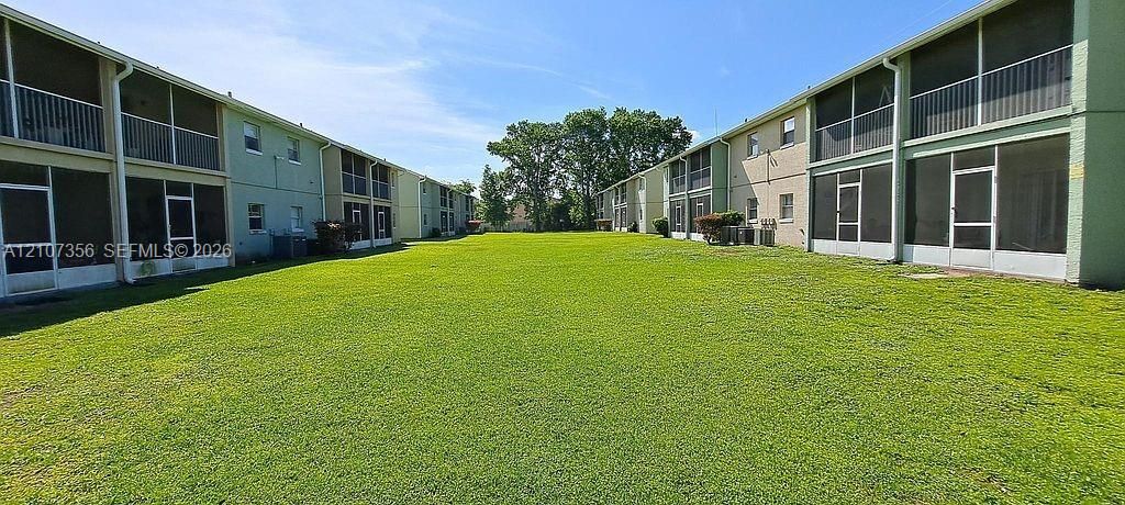 Expansive manicured lawn flanked by multi-story residential buildings featuring screened-in patios and balconies