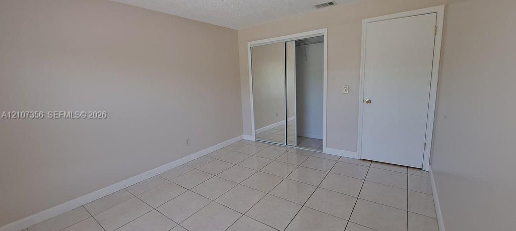Bedroom #2 Neutral-toned interior space featuring large-format ceramic tile flooring, sliding mirrored closet doors, and a solid-core interior door