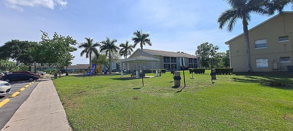 Common grounds featuring a grass lawn, mature palm trees, a covered pavilion, BBQ Grills and a playground structure