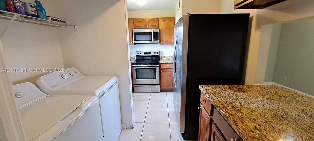 Kitchen featuring wood cabinetry, Granite countertops, and stainless steel appliances, paired with a laundry area including built-in shelving and tile flooring