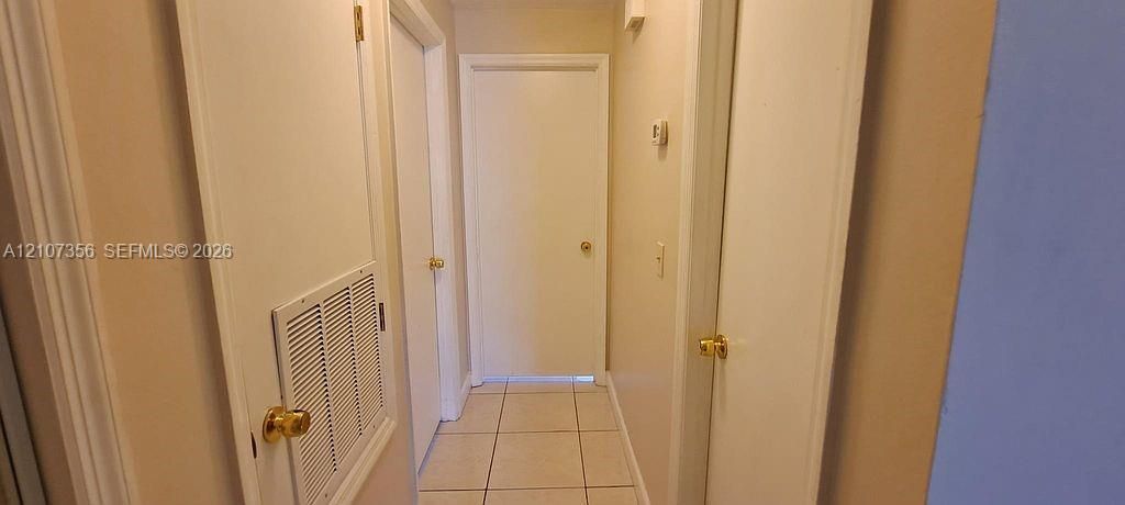 Hallway to Bedrooms Neutral-toned interior hallway featuring tile flooring, four-panel interior doors, and brass-finish hardware
