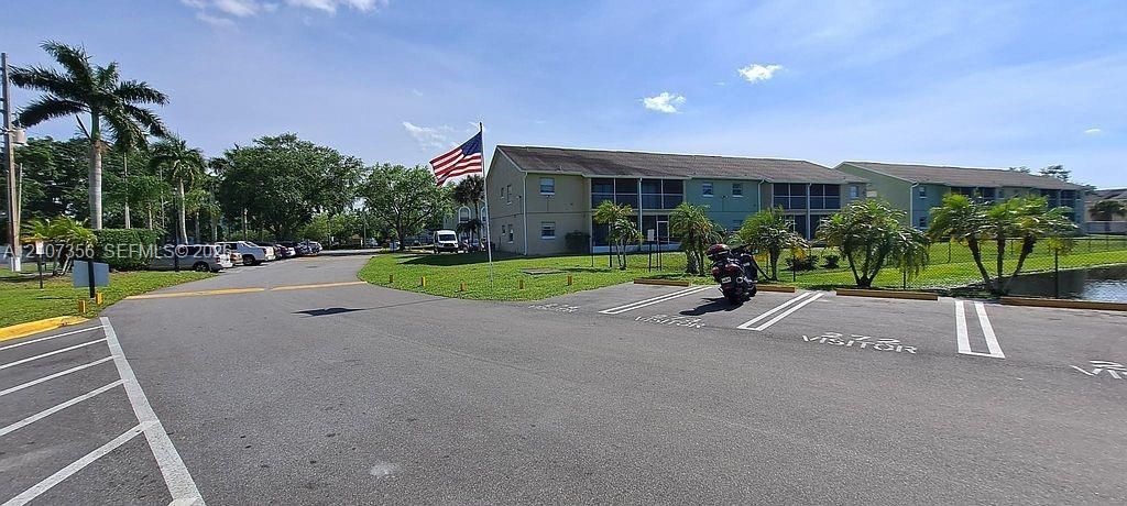 Multi-level residential building exterior featuring screened-in balconies, paved parking area, with plenty of visitor parking and landscaped grounds with mature palm trees