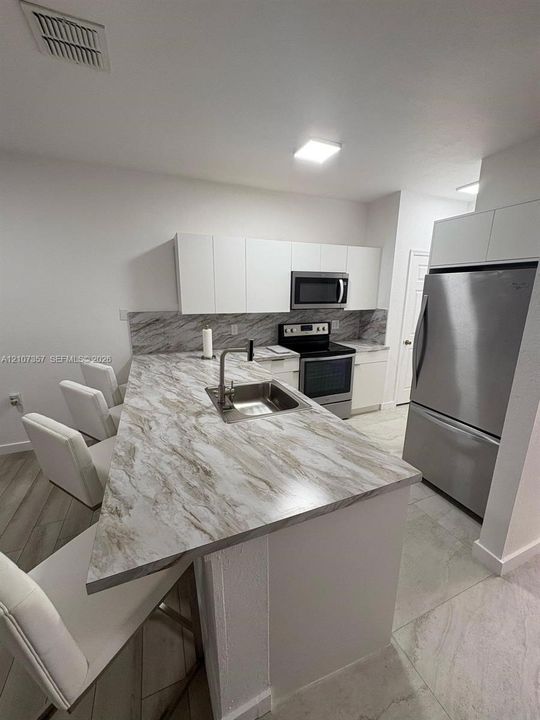 Kitchen featuring a stone-patterned peninsula with an integrated sink, white flat-panel cabinetry, stainless steel appliances, and large-format tile flooring