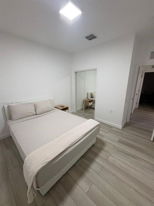 Interior space featuring wood-finish flooring, white walls, and a closet with sliding mirrored doors
