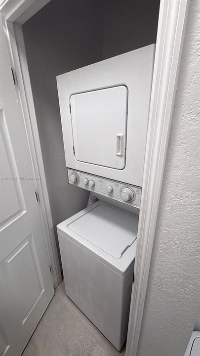 Stackable white laundry unit housed within a dedicated closet featuring a solid-core door and neutral wall finishes