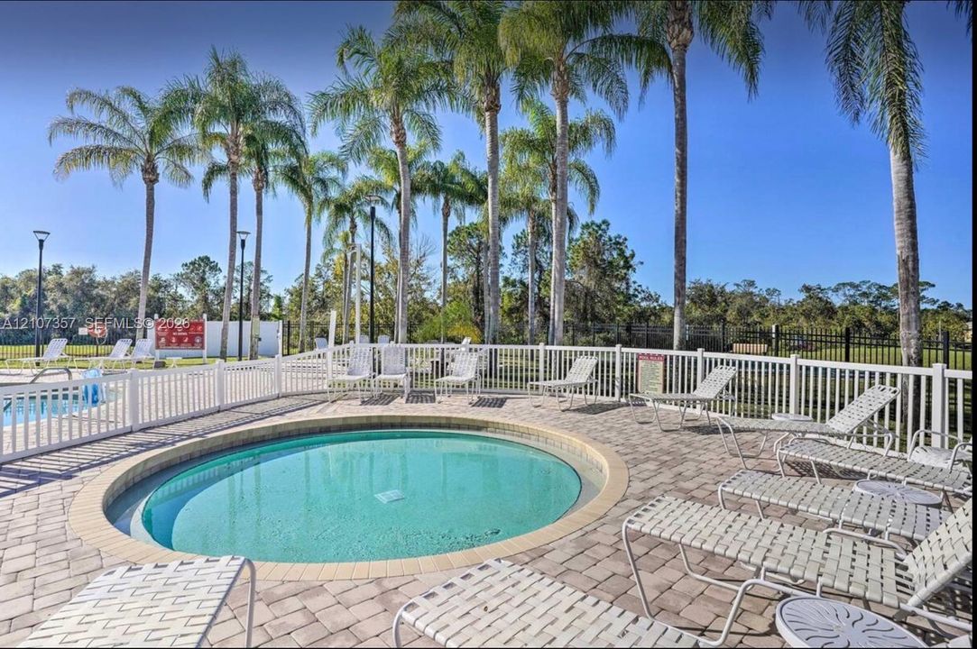 Circular in-ground spa with paver decking, enclosed by white vinyl fencing and mature palm trees