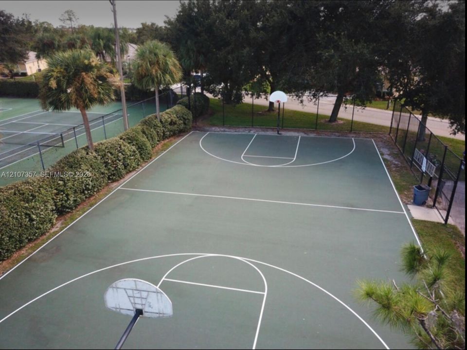 Outdoor recreational area featuring a paved basketball court with dual hoops and a fenced tennis court perimeter