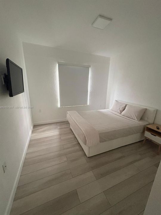 Neutral-toned interior featuring wood-finish flooring, white walls, and a window fitted with a roller shade