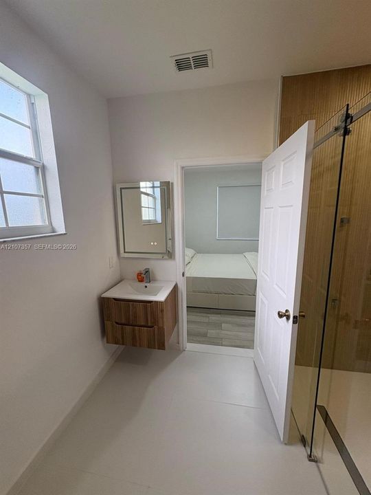 Bathroom featuring a wall-mounted vanity with wood-finish cabinetry, an integrated sink, a rectangular mirror, and a glass-enclosed shower